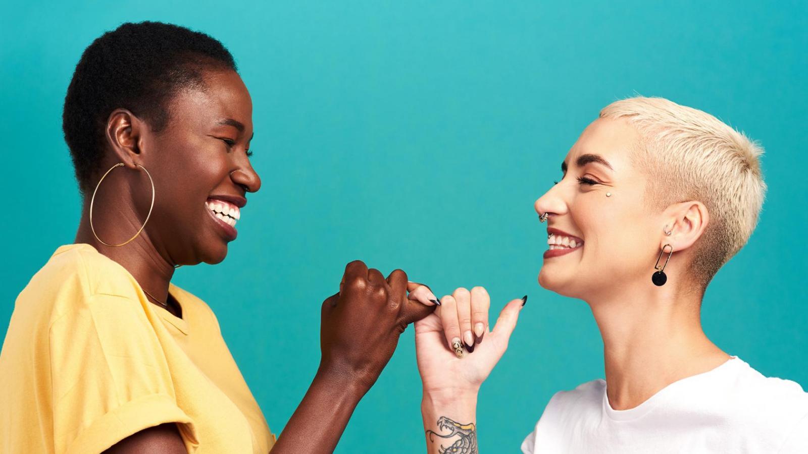 Studio shot of two young women linking their fingers against a turquoise background