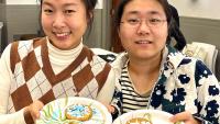 Two students smile as they look into the camera while holding decorated sugar cookies