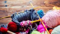 view from above on a wooden table with lots of balls of wool, knitting needles and other tools.